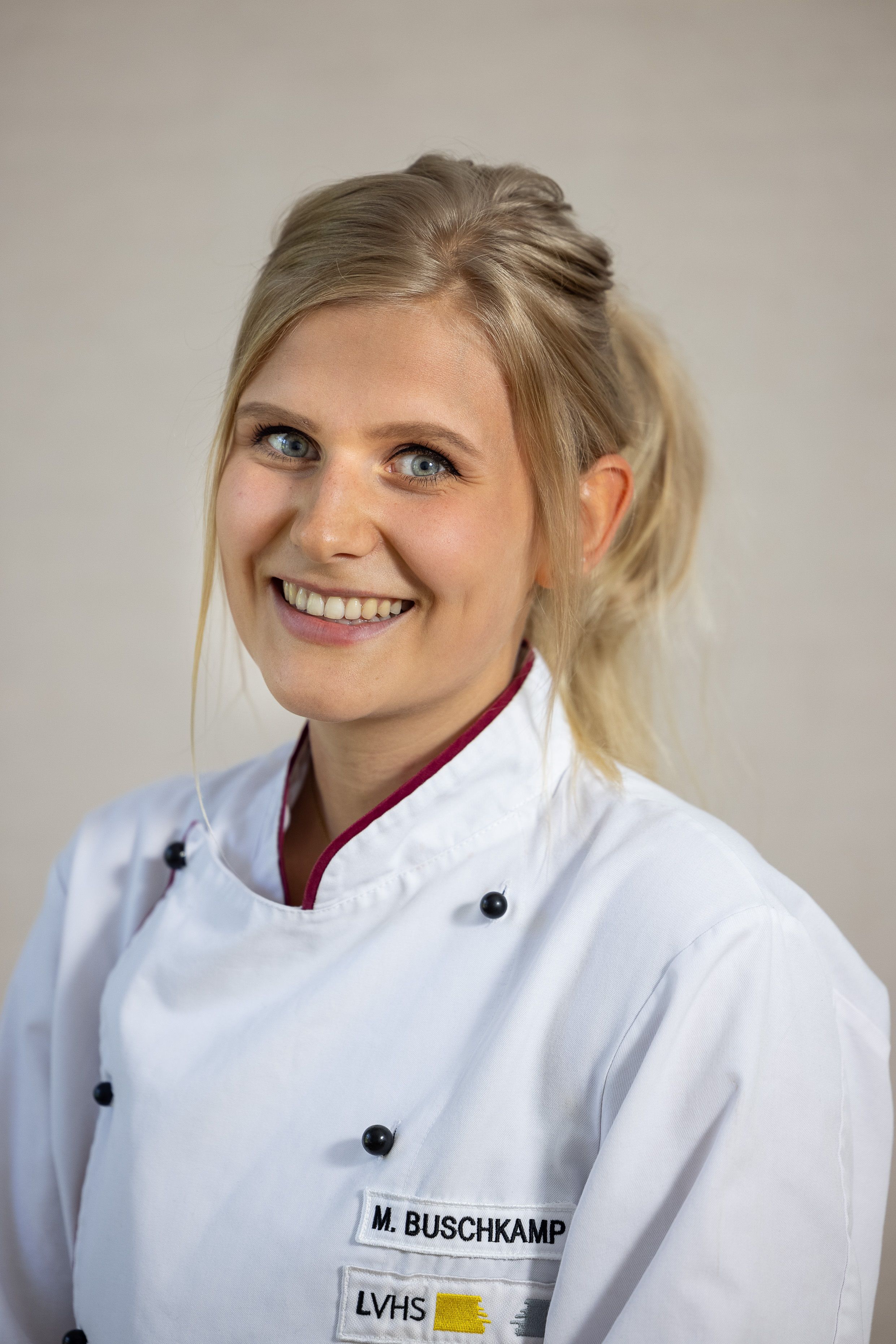 Lächelnde Köchin im weißen Chefjacke mit Namensschild „M. Buschkamp“.